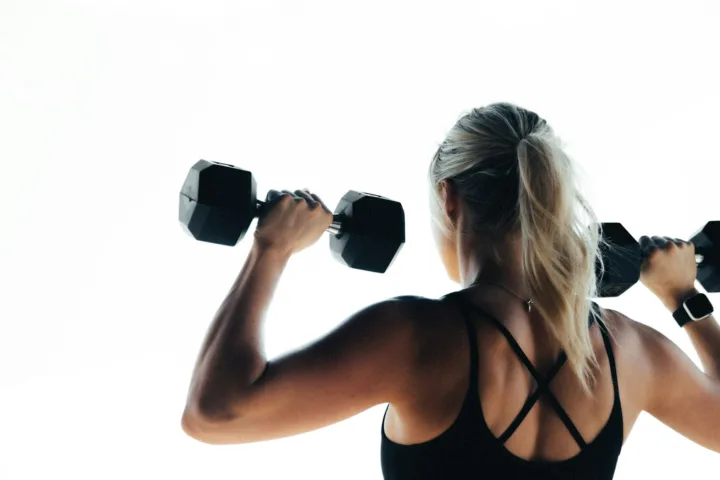 Woman doing a dumbbell shoulder press, seen from behind