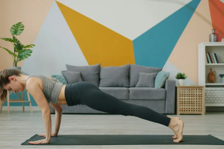Woman holding a plank on a yoga mat in a living room