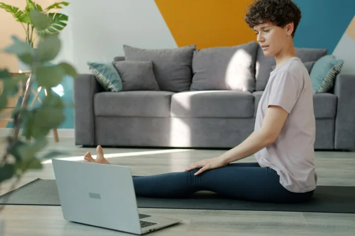 Woman following a home workout video on her laptop while stretching on a yoga mat