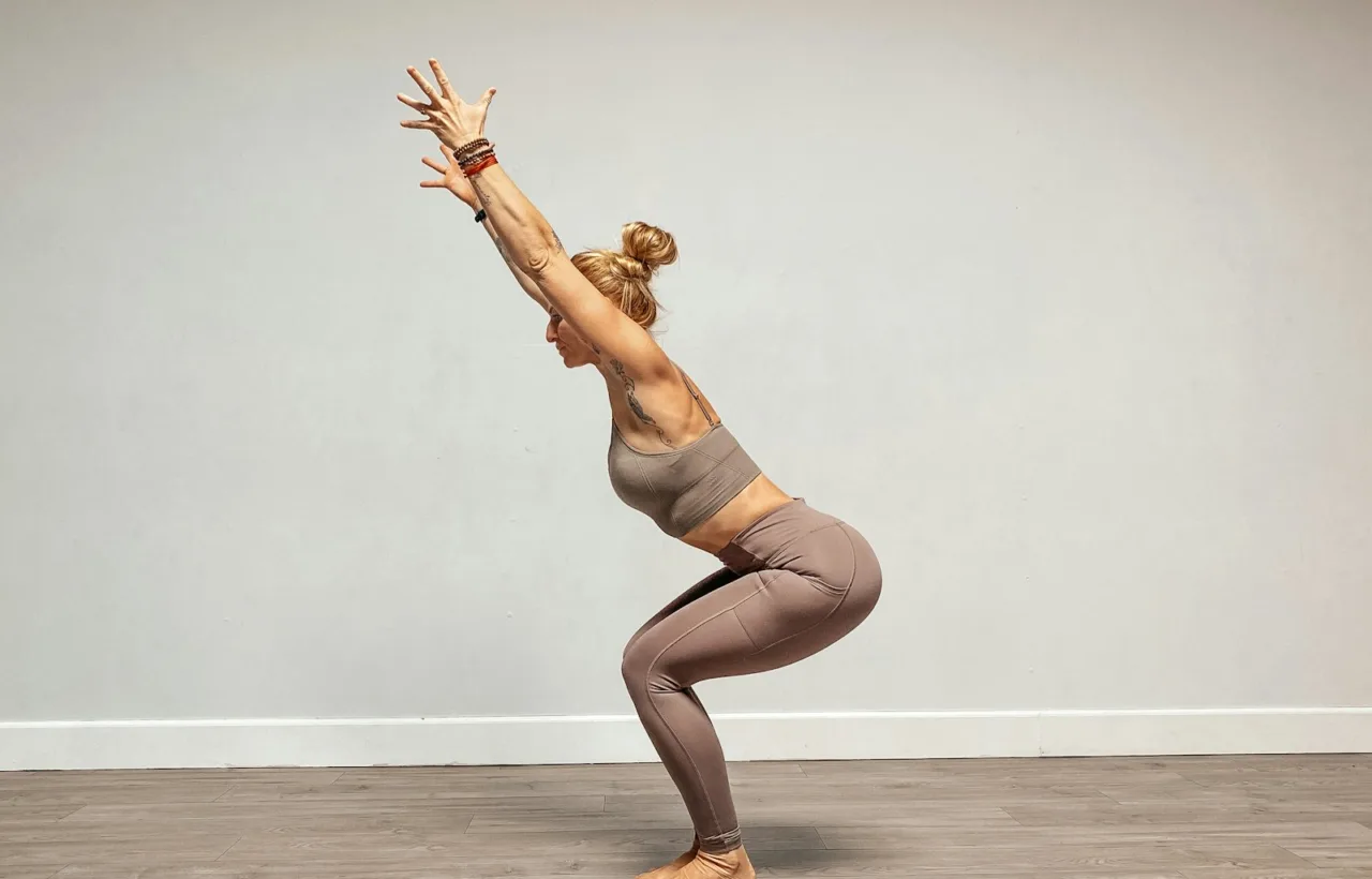 Woman holding a bodyweight squat with her arms raised